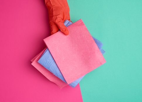  viscose rag for cleaning dust in the house in hands with an orange glove on, colored background