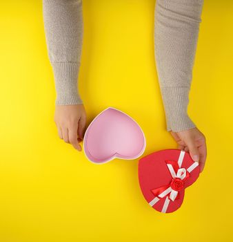 two female hands holding an open red heart-shaped box, festive backdrop, yellow background 