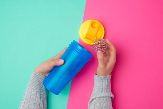 plastic blue shaker bottle with a yellow cap and an iron ball for sports people on a colored background, top view