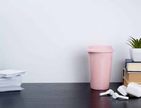 wireless white headphones with charging, pink ceramic cup with coffee and white sheets for notes on a black table, workplace