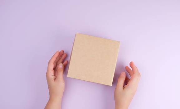 girl hold a brown square box on a purple background, top view, concept of giving gifts