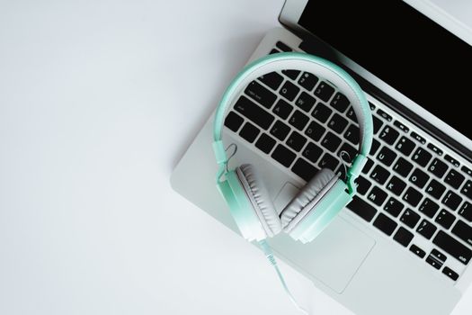 Top view of headphones with computer laptop on white office desk for entertainment and leisure online concept