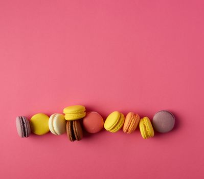 round multi-colored baked macarons with cream lie in a line on a red background, flat lay, copy space 