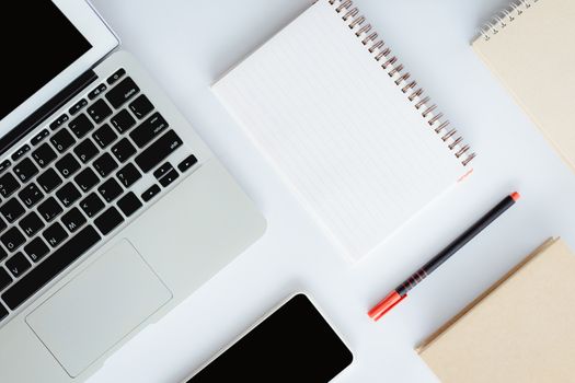 Top view of white office desk with laptop computer, smartphone, notebook and a pen for business and workspace concept