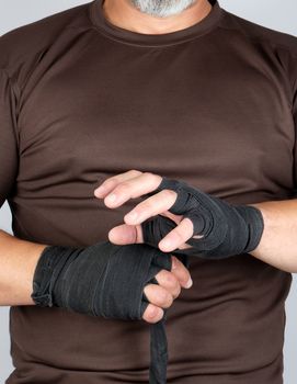 man wraps his hands in black textile bandage for sports, white background, close up