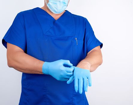 male doctor in blue uniform puts on his hands blue sterile latex gloves before surgery, white background