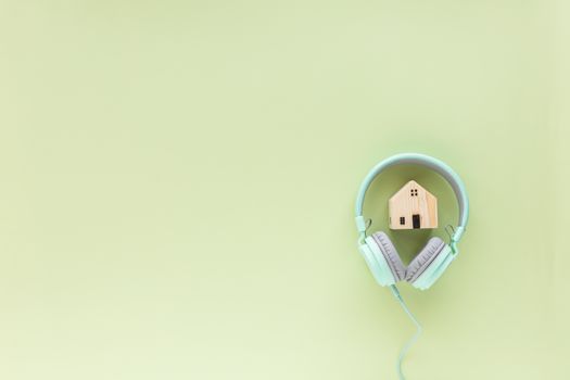 Green headphones with wooden house model on green background with copy space for time to relax,  self-quarantine, staying home and social distancing in coronavirus or Covid-19 outbreak situation
