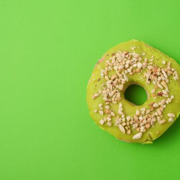 round baked donut with green pistachio glaze sprinkled with crushed nuts, green background, feed on top