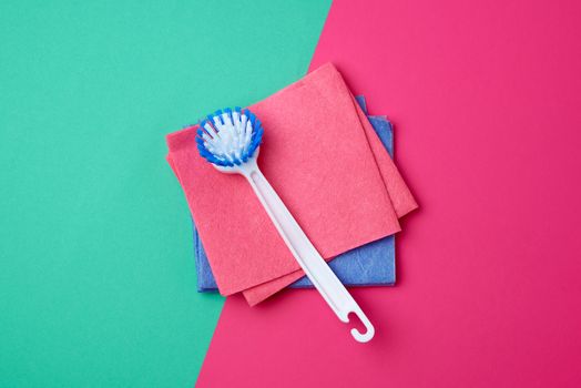 plastic white brush with handle and multi-colored square dishwashing sponges on a pink green background, top view, flat lay