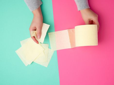 roll of yellow toilet paper in female hands, torn pieces on a colored background, top view