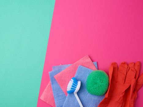 items for home cleaning: red rubber gloves, brush, multi-colored sponges for dusting on a pink green background, top view, flat lay
