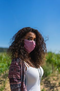 Portrait of a pretty young Brazilian woman looking at the camera with a mask protection for coronavirus infection. Concept of dangerous, loneliness in nature