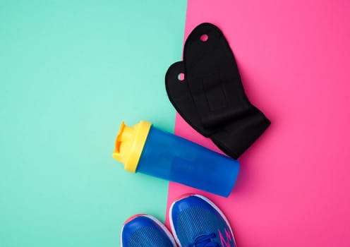 pair of sports sneakers with blue laces, plastic water bottle and black gloves on a colored abstract background, top view, place for test