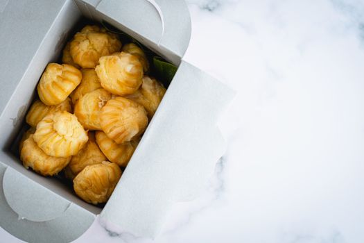 Delicious eclair vanilla cream, choux dough filled with a cream, homemade bakery in paper box packaging on white marble background for snack eating concept