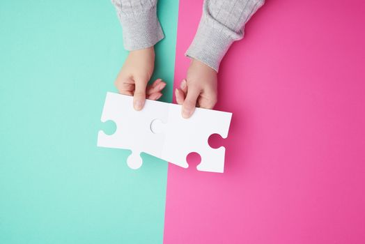 two empty paper white pieces of puzzles in female hands, puzzle connected, colorful background, top view