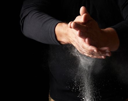 man claps his hands and scatters to the side a white substance on a black background, magnesia for rubbing hands, selective focus