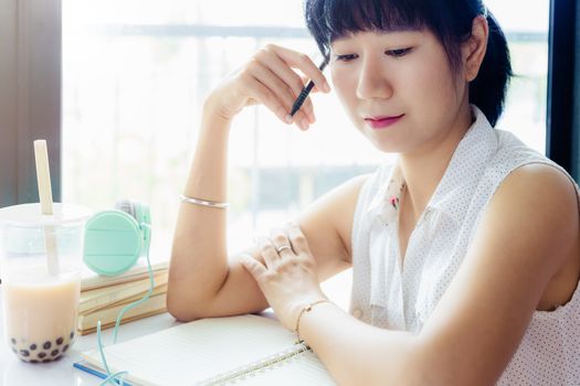 Asian woman holding a pen and thinking about work with a plastic cup of bubble tea against blurred background for staying and working at home concept