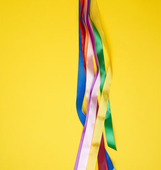 many silk multi-colored ribbons on a yellow background, top view