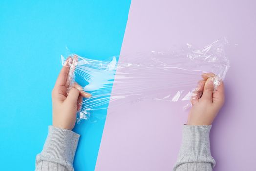 two hands hold a piece of transparent plastic film on a colored background, top view