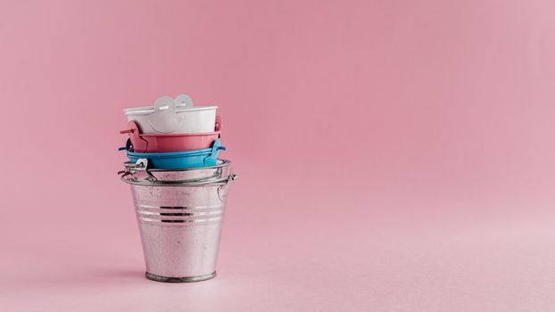 Mini colored tin pails or buckets on pink background with copy space for household items concept