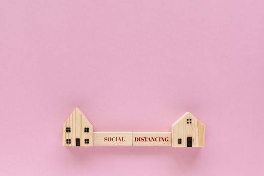 Wooden house model with social distancing text on pink background for self-quarantine and staying home in coronavirus or Covid-19 situation concept