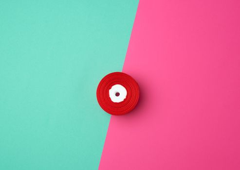 spools with red satin ribbon on a green pink background, top view