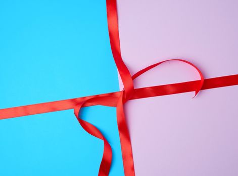 red satin ribbon on a colored background, imitation of tying and packing a gift