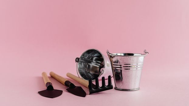 Gardening tools with colored tin pails or buckets on pink background for planting concept