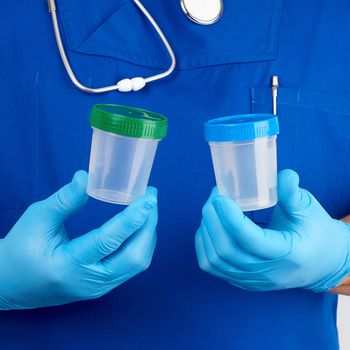 doctor in blue uniform and latex gloves is holding an empty plastic container for taking urine samples, concept of timely diagnosis