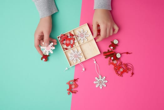 two female hands and wooden carved Christmas decorations for the holiday tree, pink green background 