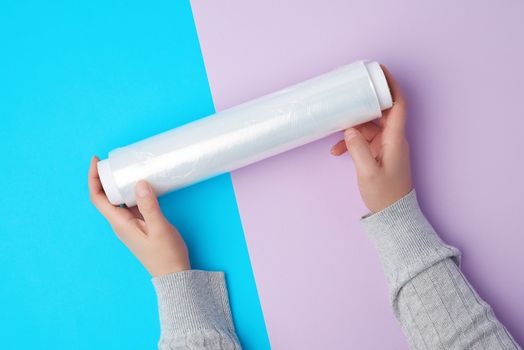 two hands hold a large roll of wound white transparent film for wrapping food, top view