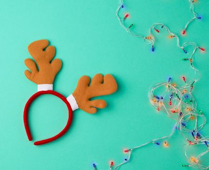 burning christmas garland on a white wire with colorful lights and carnival deer head mask on a green background