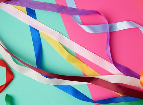 many silk multi-colored ribbons on a colored background, top view