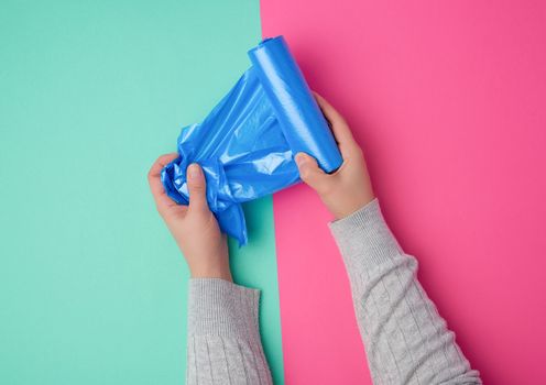 female hand unwinds a blue plastic bag for rubbish, green pink background