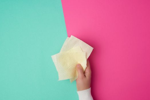 yellow toilet paper in female hands, torn pieces on a colored background, top view