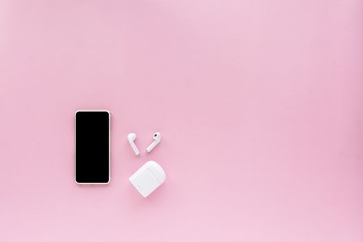 Smartphone with wireless headphones on pink background with copy space for media technology and modern lifestyle concept