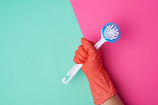 white plastic cleaning brush in hand, protective orange glove on hand, color background