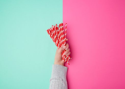 hand holds a stack of red paper tubes for a cocktail on a multi-colored background, concept of rejection of plastic and the use of recyclable materials