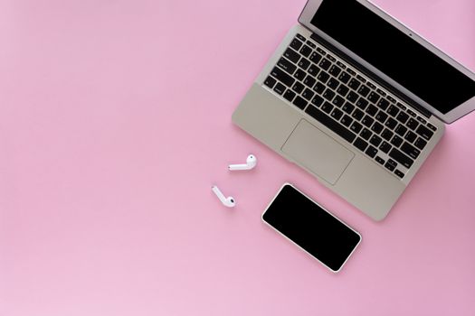 Computer laptop and smartphone with wireless headphones on pink background with copy space for media technology and modern lifestyle concept