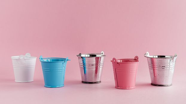 Mini colored tin pails or buckets on pink background with copy space for household items concept