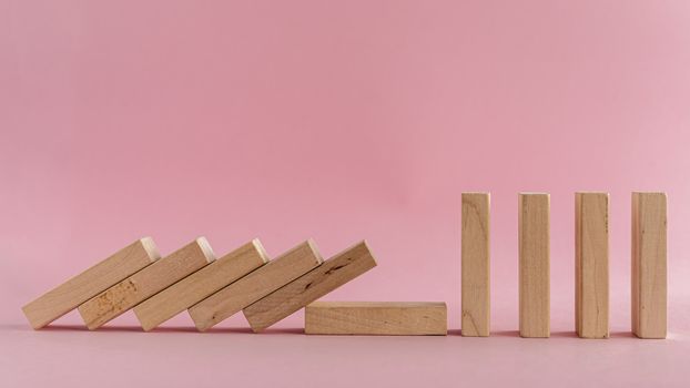 The wooden toys falling down but the next others that is far away could stand on pink background for social distancing concept