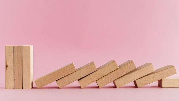 The wooden toys arranged in a horizontal row but the next others falling down on pink background for leisure activities concept