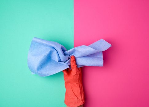 blue viscose rag for cleaning dust in the house in hands with an orange glove on, colored background
