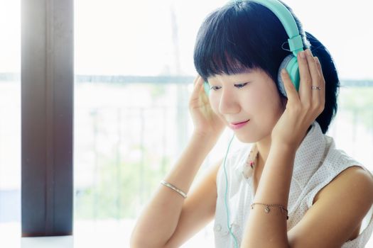 Asian woman wearing headphones and listening music with blurred background for entertainment, relaxation and stay at home concept