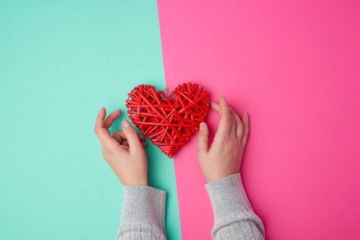 two female hands holding a red wicker heart a symbol of love on a green-pink background, top view