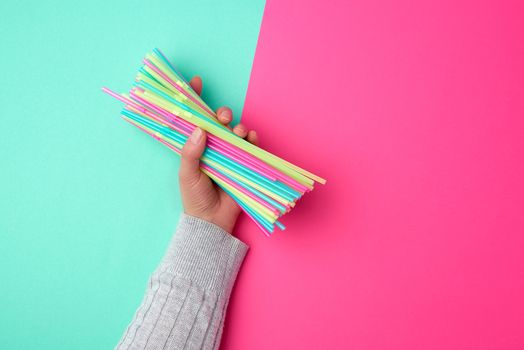 female hand holding multicolored plastic cocktail tubes, green pink background