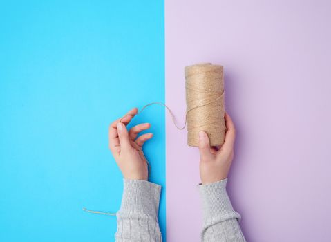 female hands holding a skein with brown eco thread on a colorful background, top view