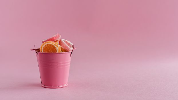 Full of colourful fruit Jelly candy in a pink bucket against pink background for food and snack concept