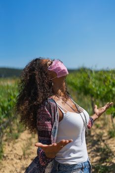 Portrait of a pretty young Brazilian woman looking up with a mask protection for coronavirus infection. Concept of anxiety, frustration, depression and loneliness outdoors.