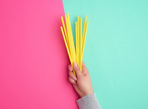 hand holds a stack of yellow paper tubes for a cocktail on a multi-colored background, concept of rejection of plastic and the use of recyclable materials